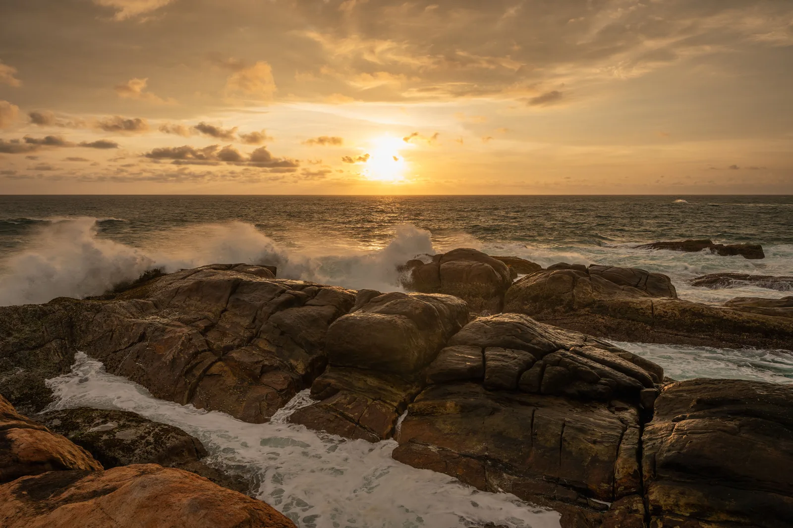 A calm sea and orange sky at sunset on the rocky south coast near Unawatuna