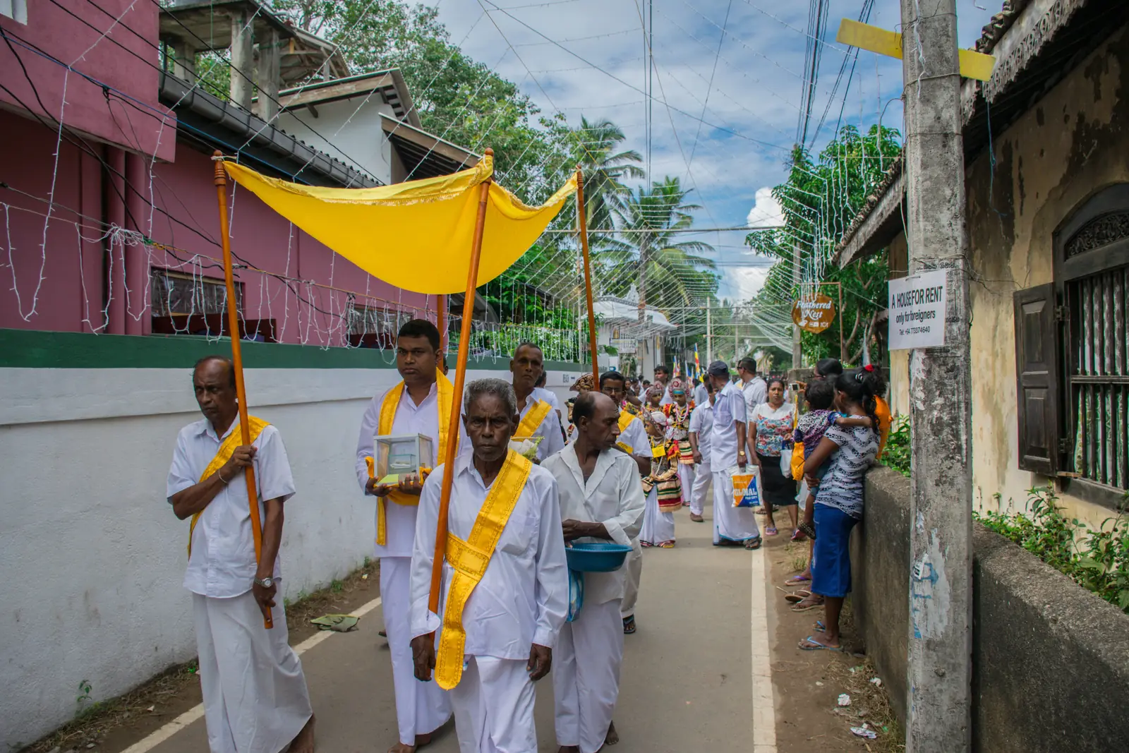A Poya day procession of devotees in white carrying a yellow canopy banner