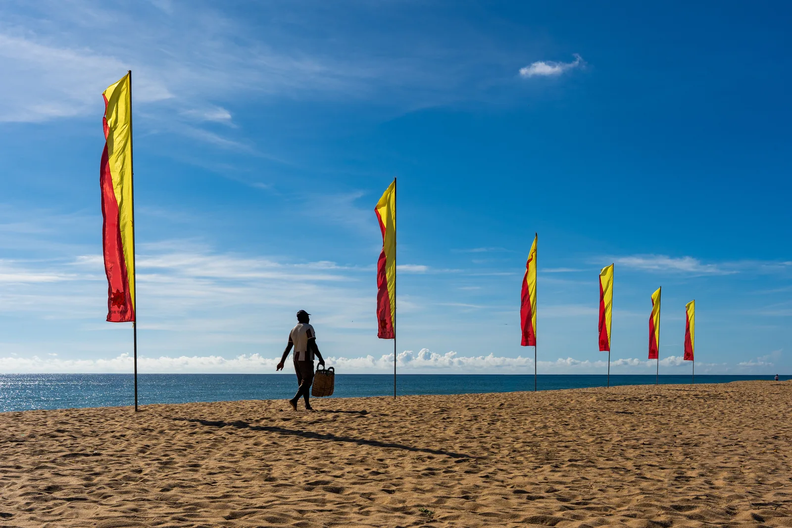 Sri Lanka in July: one walker between red and yellow flags on the empty sand at Batticaloa beach