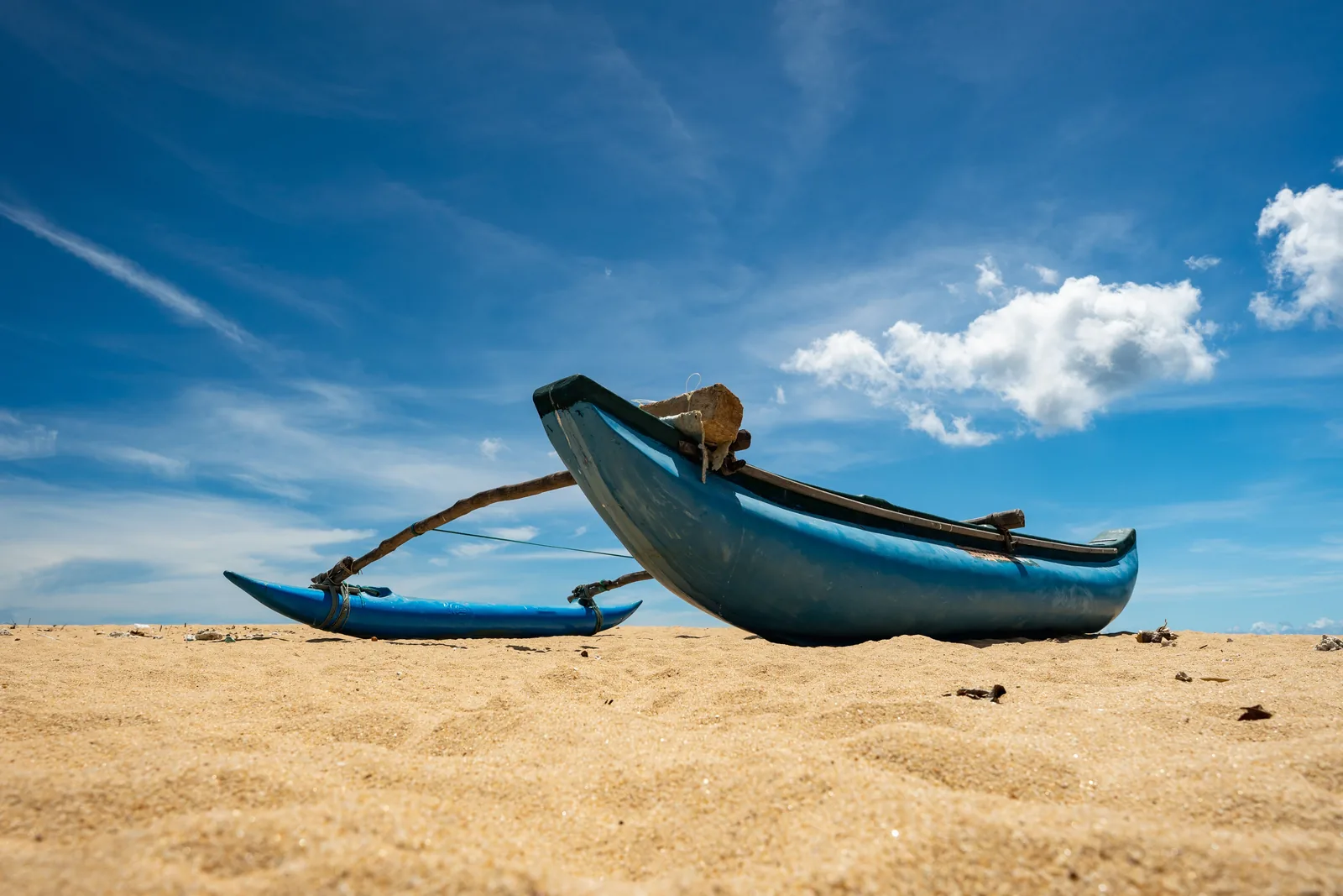 Two blue traditional fishing canoes resting on empty sand on Sri Lanka's east coast