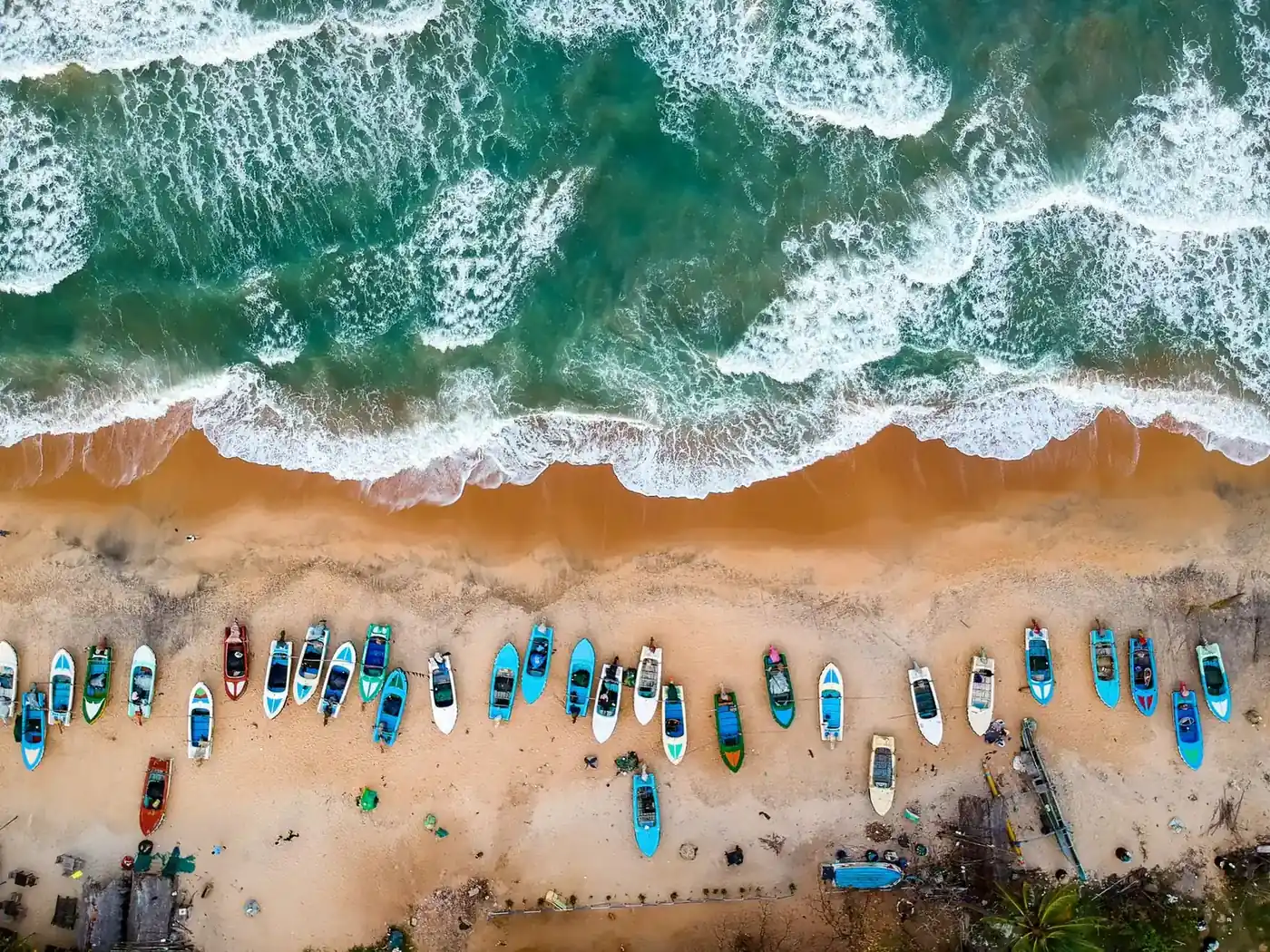 An aerial view of fishing boats lined up on a beach with the swell breaking behind them in the sri lanka monsoon season