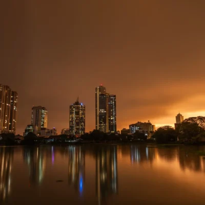 Colombo skyline at dusk under a heavy orange overcast, reflected in Beira Lake, in the sri lanka monsoon season