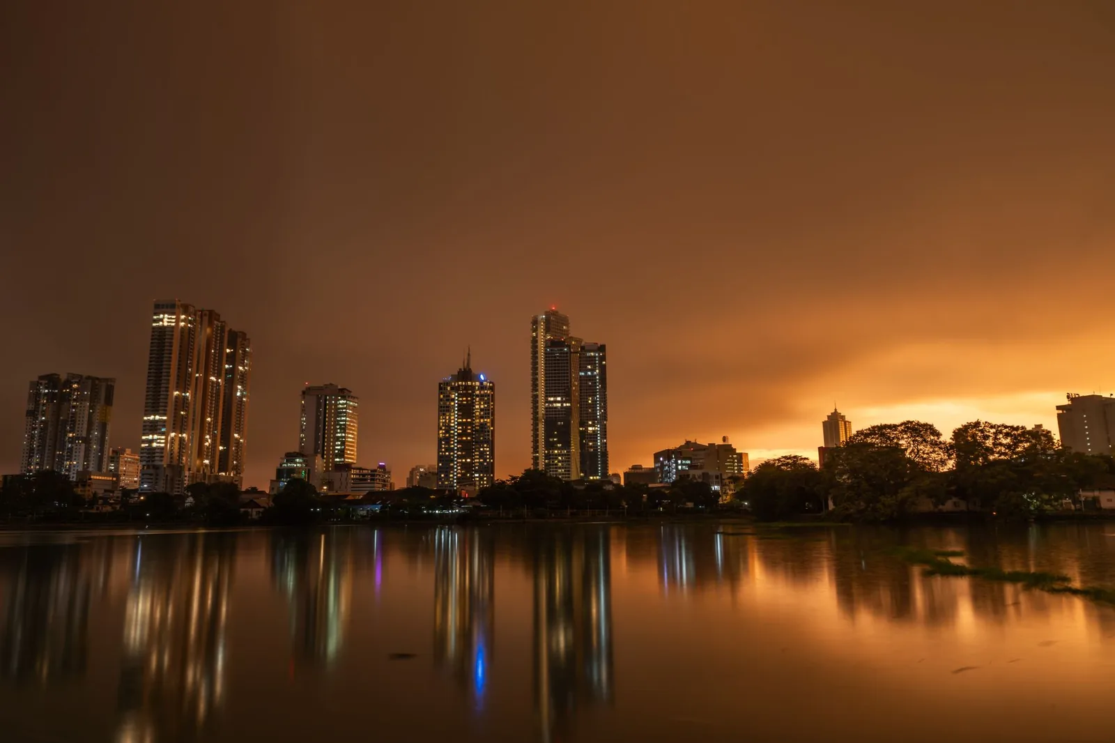 Colombo skyline at dusk under a heavy orange overcast, reflected in Beira Lake, in the sri lanka monsoon season